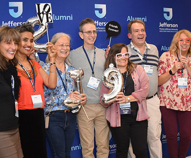A group photo of Jefferson alumni at an event posing together with fun props like sunglasses and balloons.