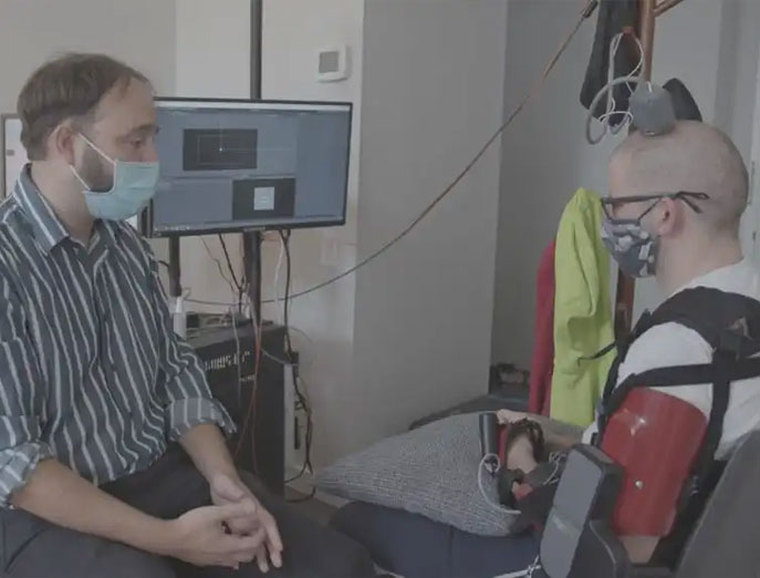 Dr. Serruya sits across from Aaron while working with him to control the arm brace while the electrodes connected to Aaron’s head are hooked up to a nearby monitor.