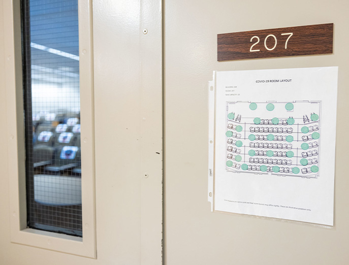 The exterior door to a classroom has a sign on it showing a COVID-19 room layout with blue-green dots indicating where occupants can sit while practicing social distancing. 