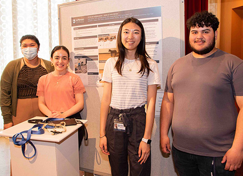 The EZ Leader Dog Leash team stands in front of a poster about their project and behind a display of the leash prototype at the 2023 Design Assistive Device Project presentation.